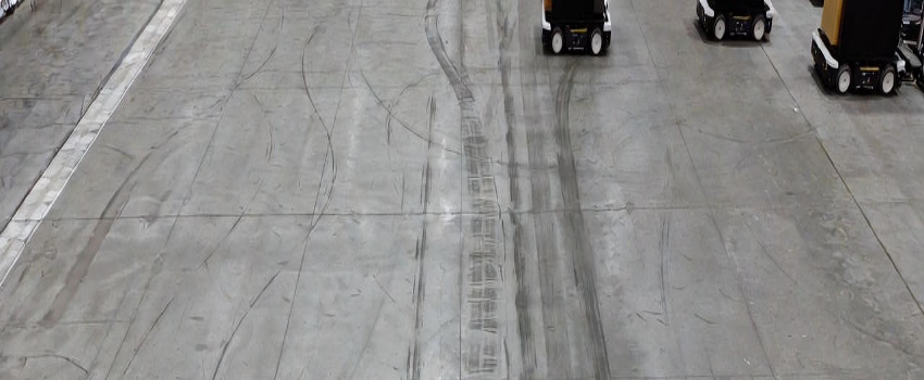 Overhead view of an automated warehouse floor showing consistent robot travel paths, illustrating how slab flatness and surface uniformity enable repeatable robotic navigation.
